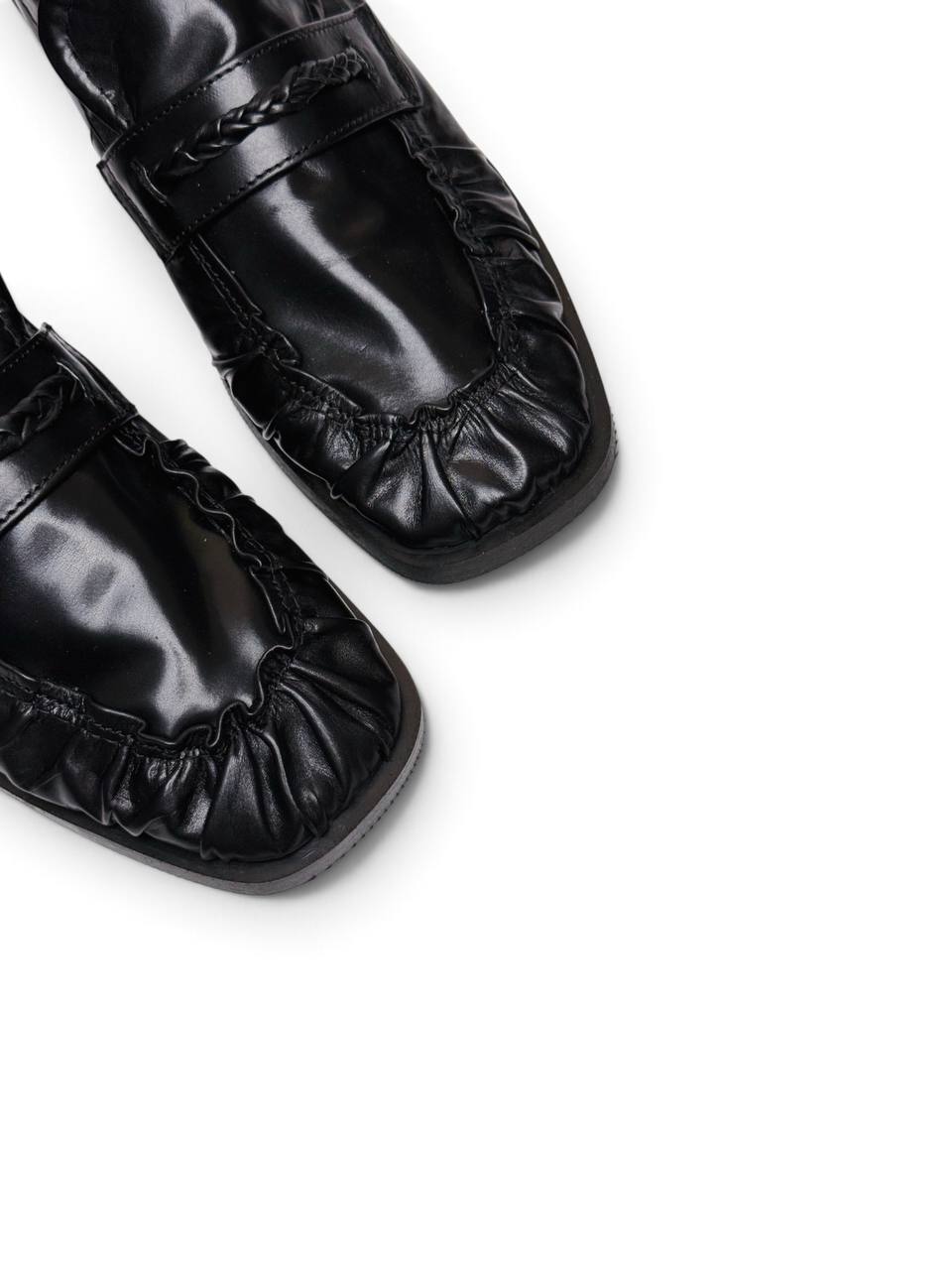 Close-up of black leather loafers showing gathered toe and braided trim