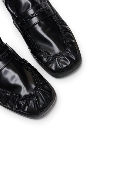 Close-up of black leather loafers showing gathered toe and braided trim