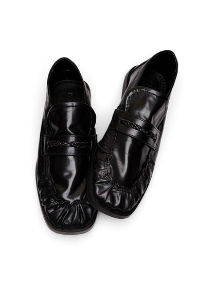 Black leather loafers viewed from above, showing braided straps
